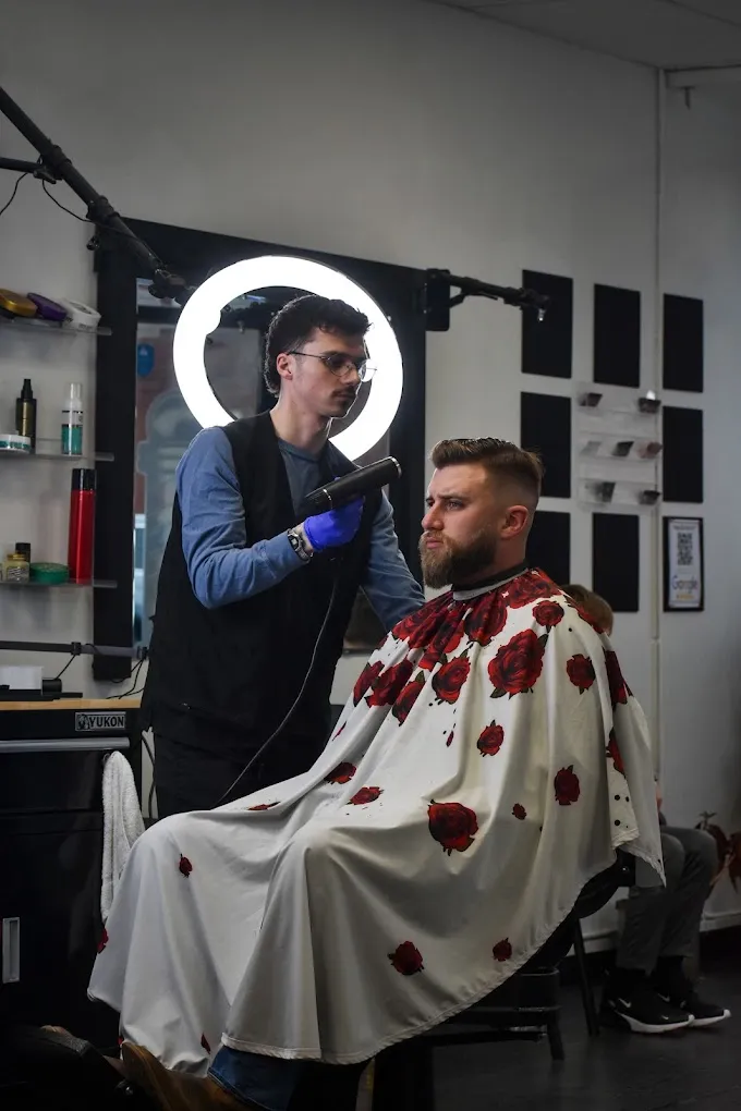 A barber at The Garage blow-drying a client’s freshly cut fade under a ring light