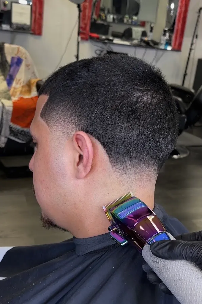 A barber using clippers to finish a mid fade, showing the blended neckline and crisp edge-up