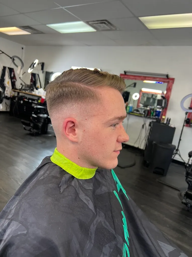 Side profile of a blonde comb-over with a hard side part, taper fade and sharp line-up